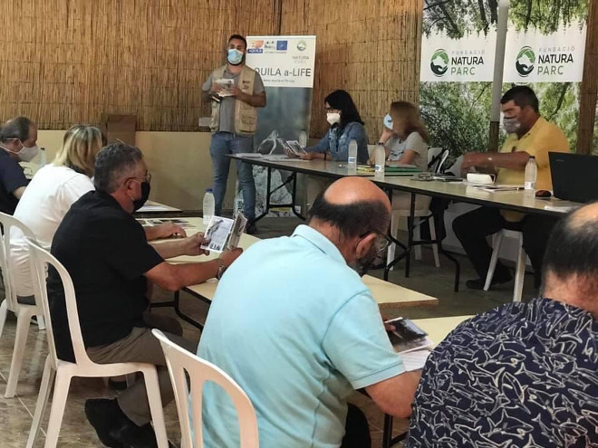 Pep Frontera realiza su intervención sobre AQUILA a-LIFE ante la asamblea de la Federación Balear de Caza, mientras sus participantes revisan el folleto del proyecto.